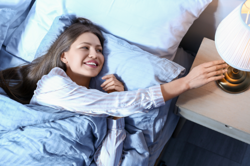 woman in bed reaching to turn off a lamp on her bedside table