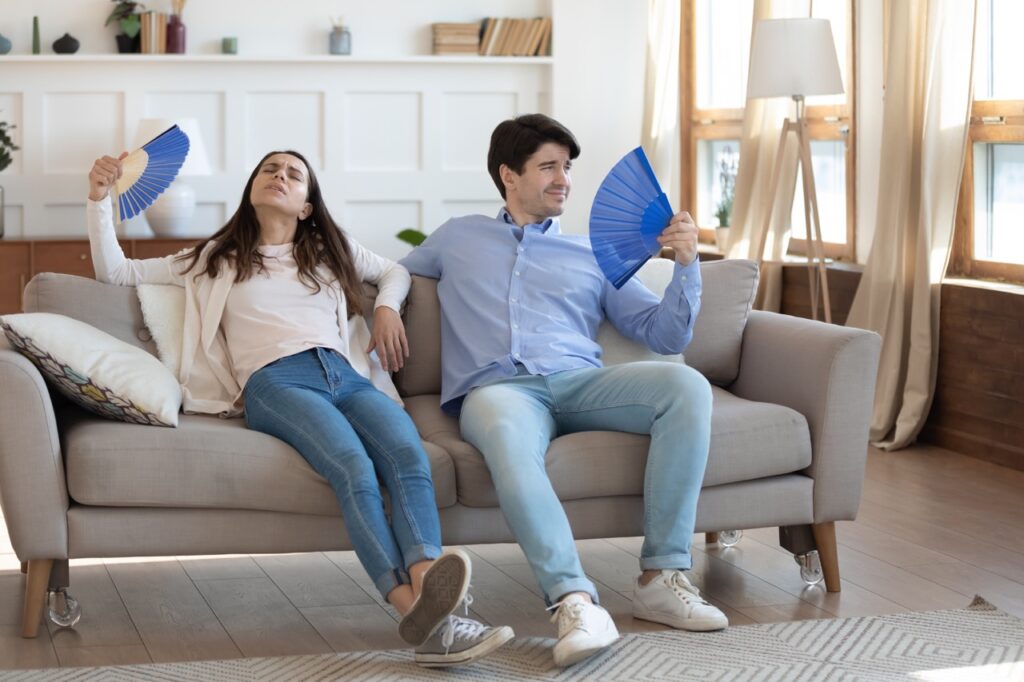 Couple sitting on couch using fans to keep cool