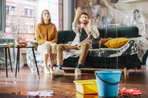 A frustrated couple dealing with a ceiling leak, with buckets catching water on the floor—highlighting the importance of a reliable leak defense system to protect homes from unexpected water damage.